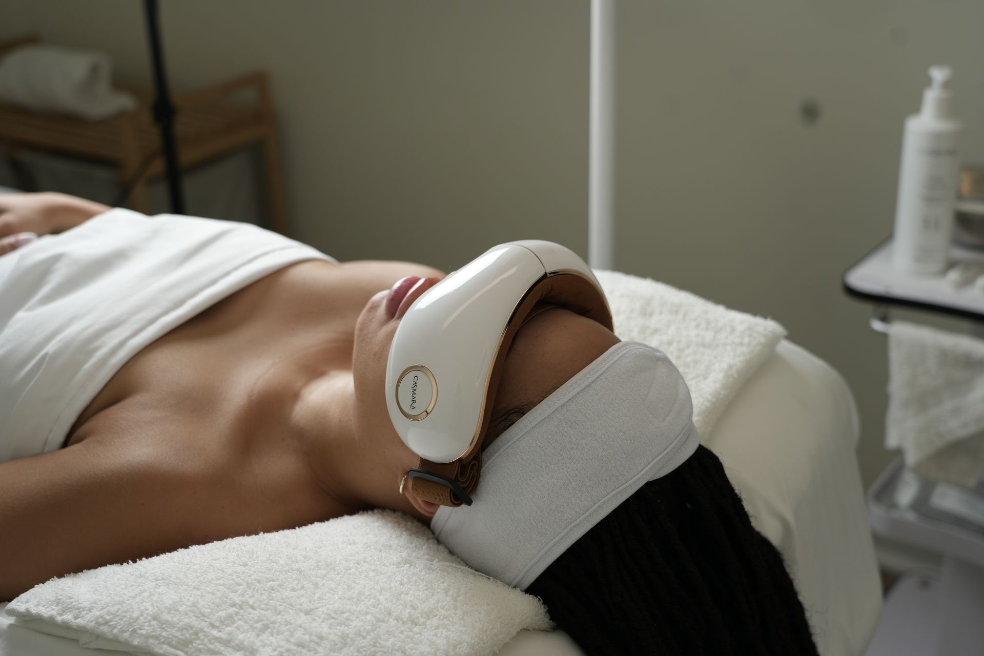 A woman is laying on a massage table with a device on her face.