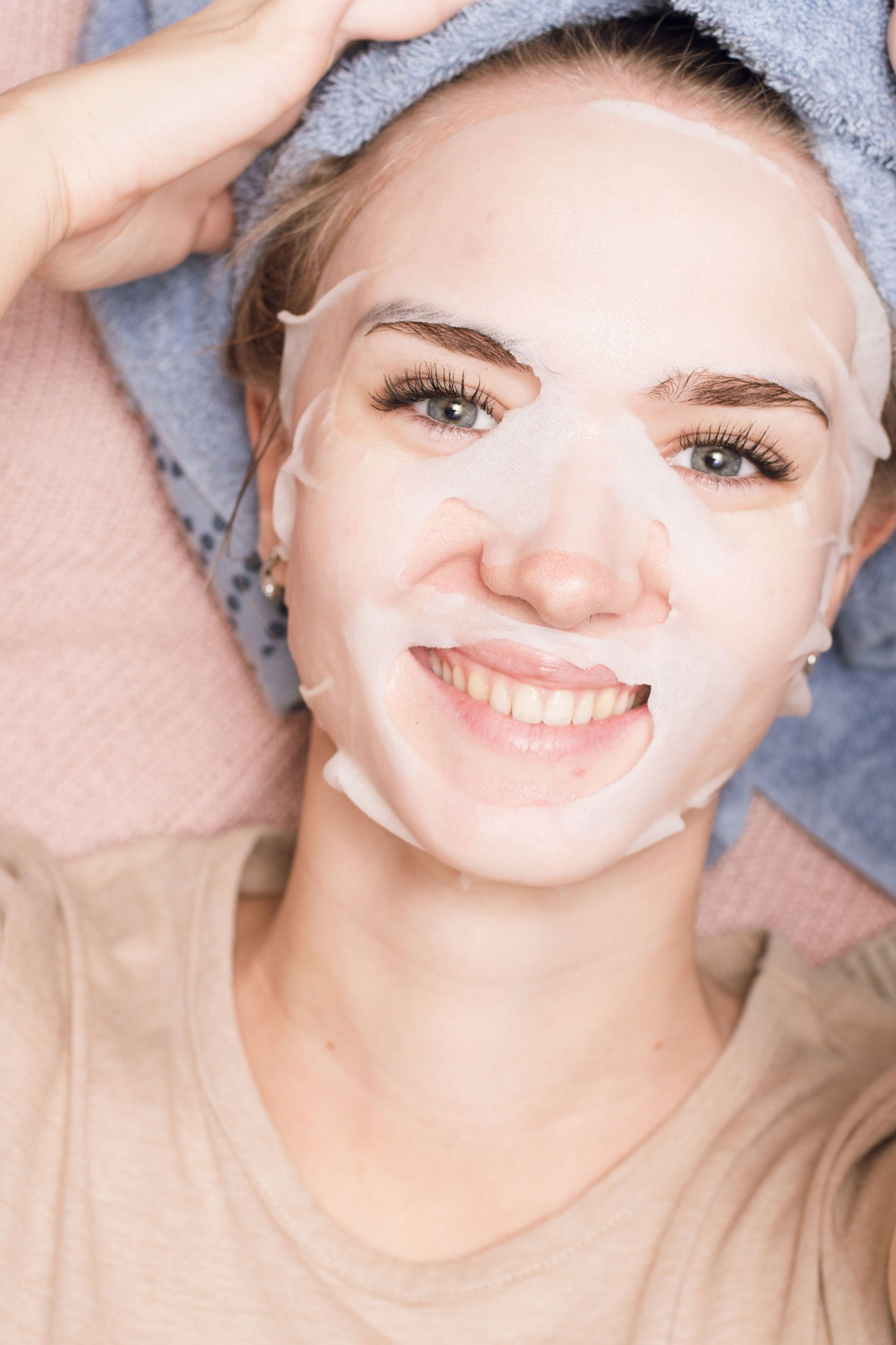 A woman is wearing a sheet mask on her face and smiling.