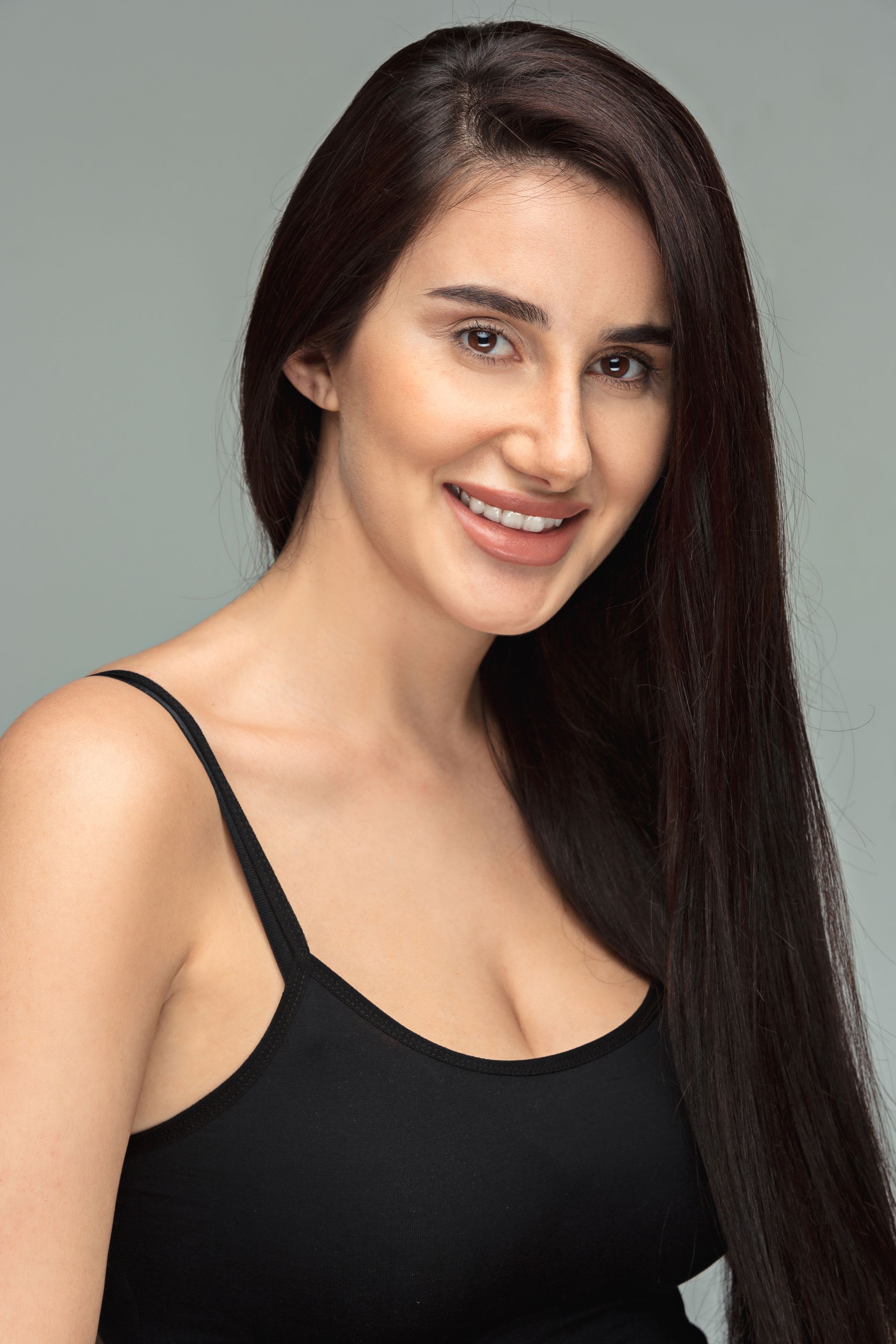 A woman with long hair is wearing a black tank top and smiling.