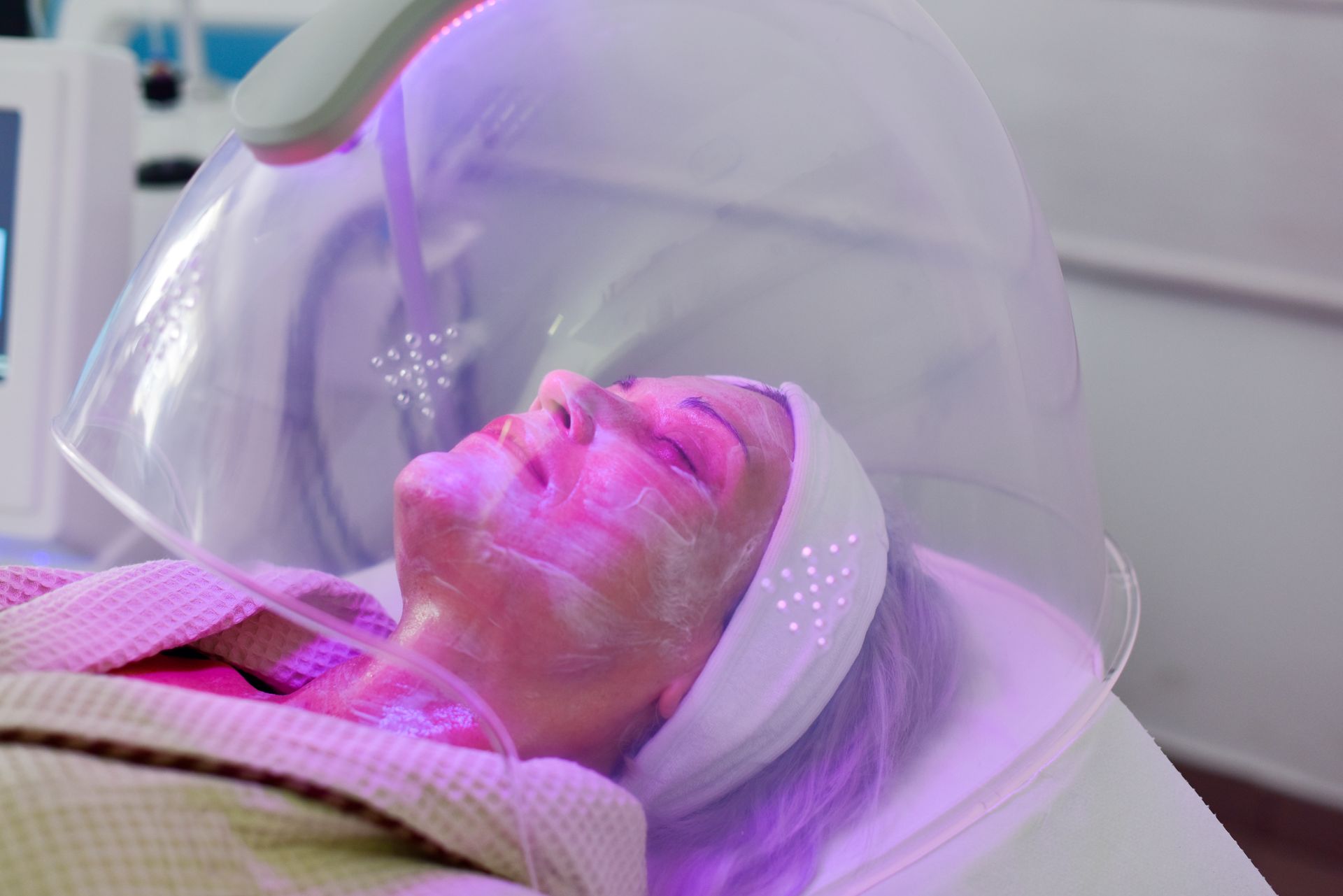 A woman is getting a facial treatment with purple lights on her face.