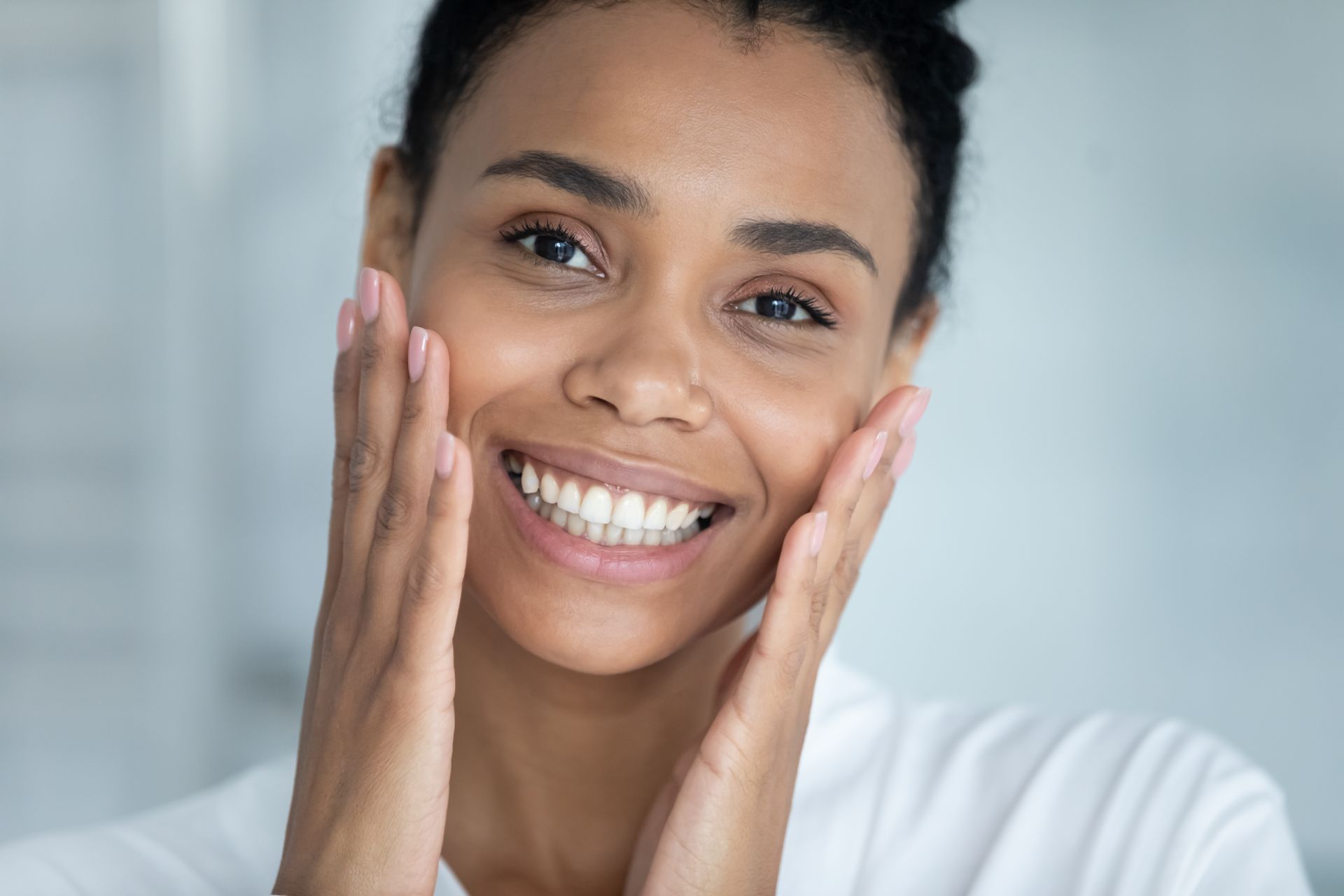 A woman is smiling and touching her face with her hands.