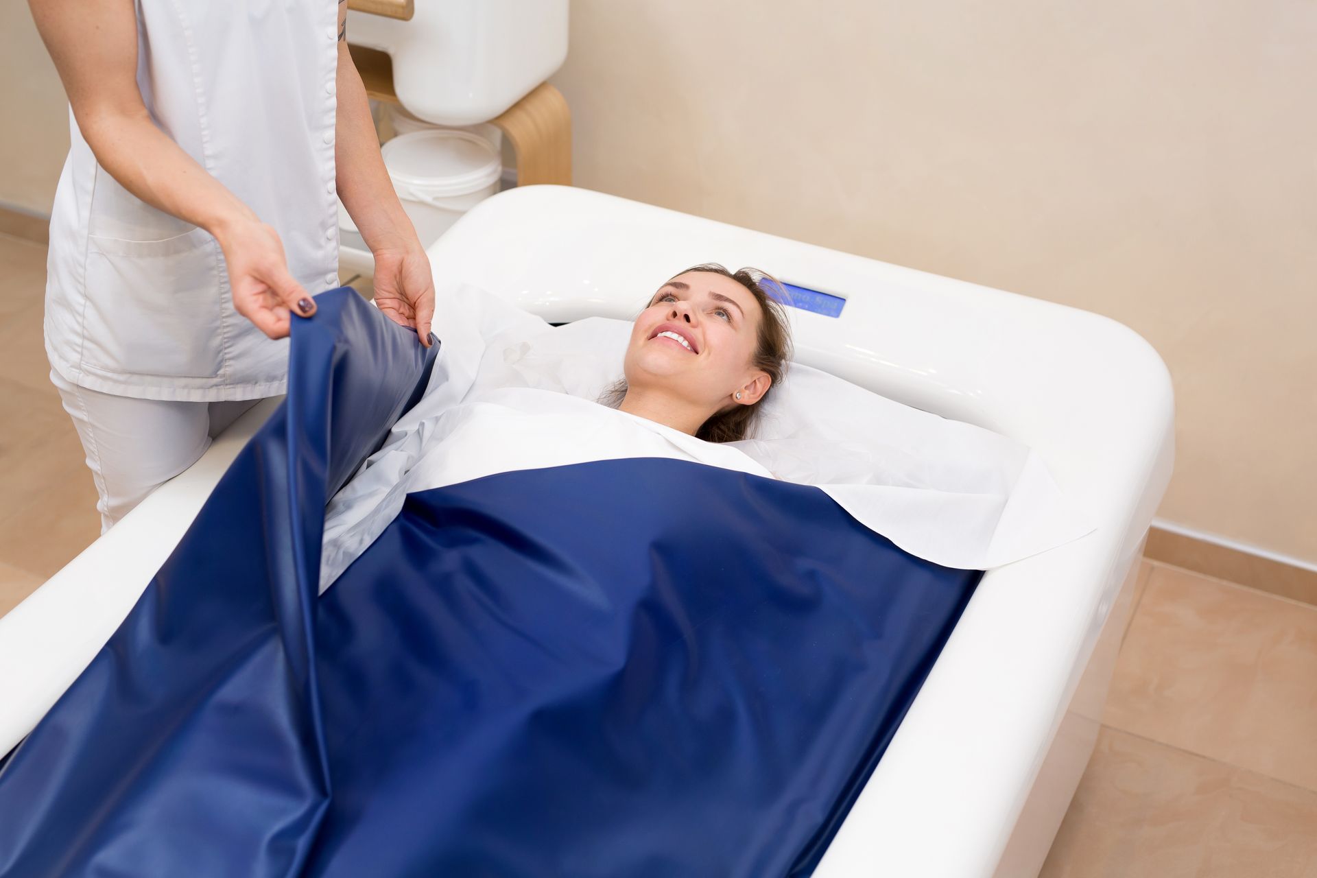 A woman is laying in a bathtub with a blue blanket on her.