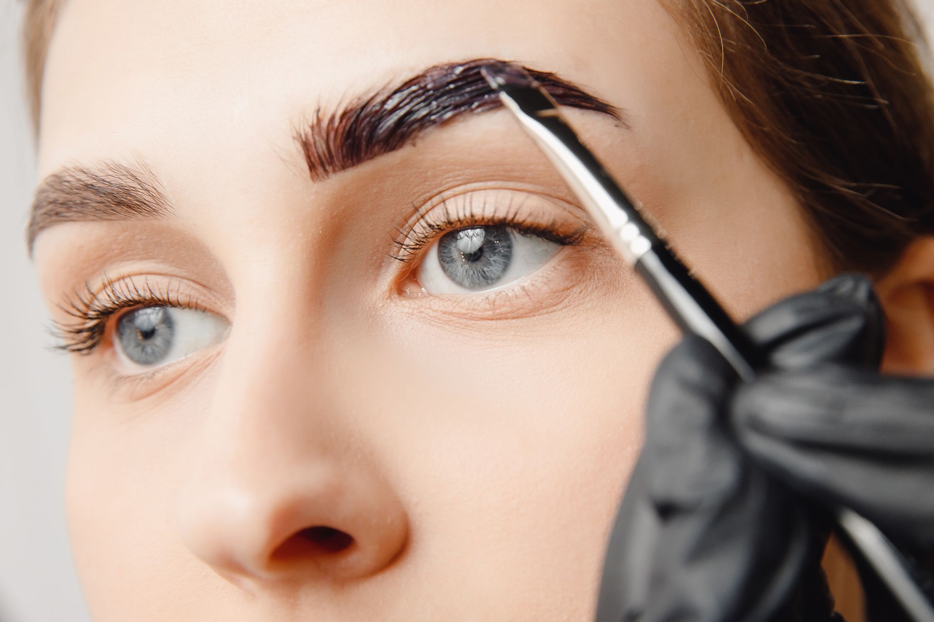 A woman is getting her eyebrows painted with a brush.