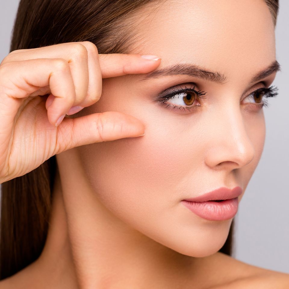 A woman is touching her eyebrow with her finger.