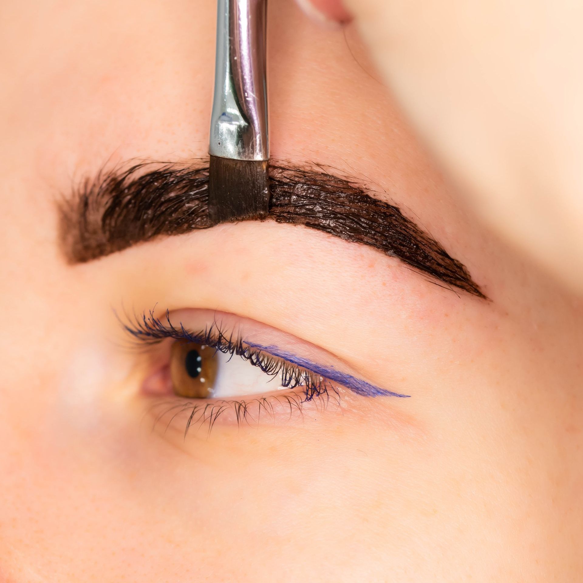 A woman is getting her eyebrows painted with a brush.