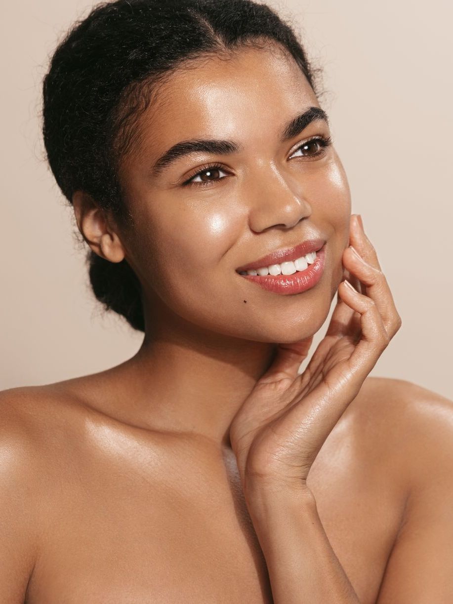 A woman is smiling and touching her face with her hands.