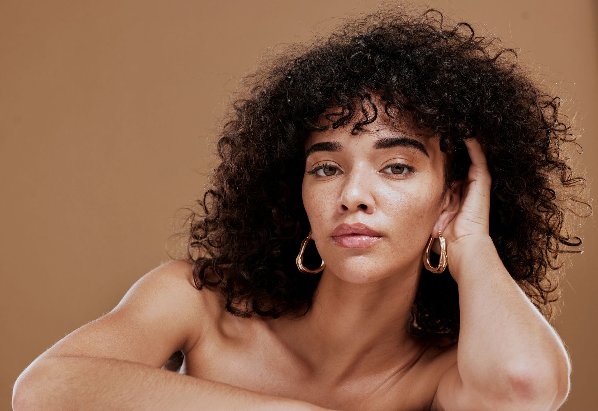 A woman with curly hair and hoop earrings is looking at the camera.