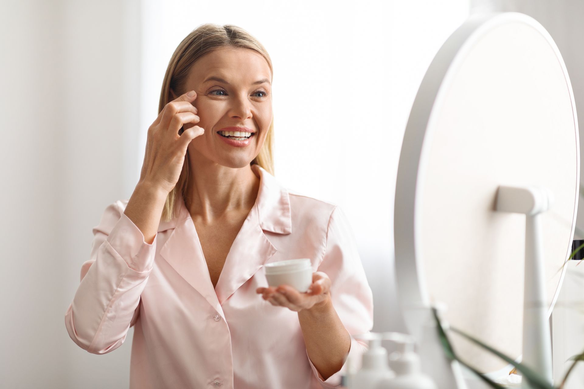 A woman is applying cream to her face in front of a mirror.