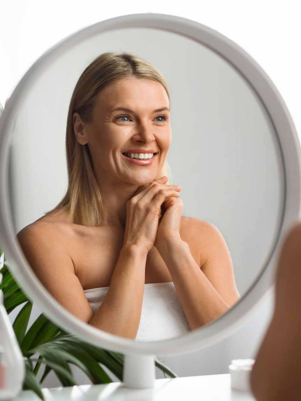 A woman is smiling while looking at her reflection in a mirror.