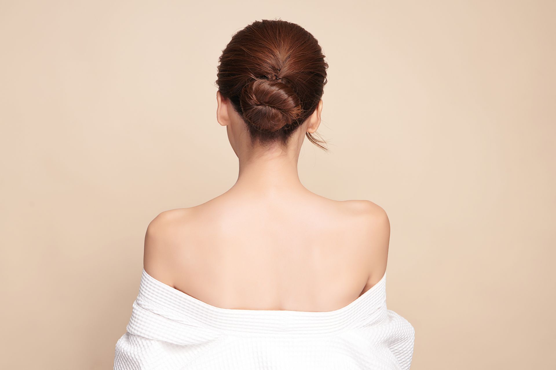 The back of a woman wearing a white robe and a bun.