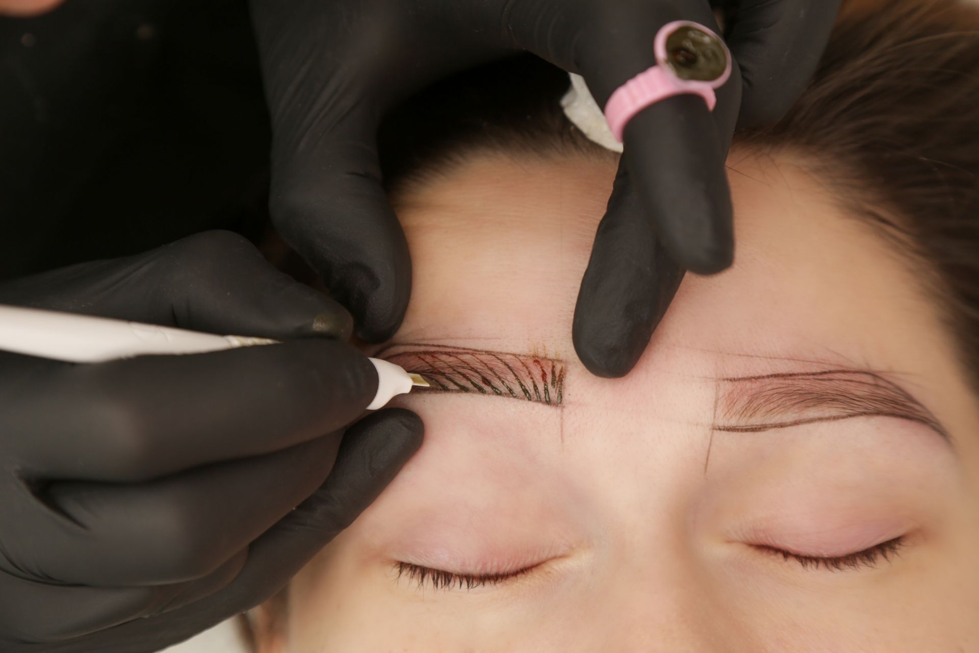 A woman is getting her eyebrows tattooed by a tattoo artist.