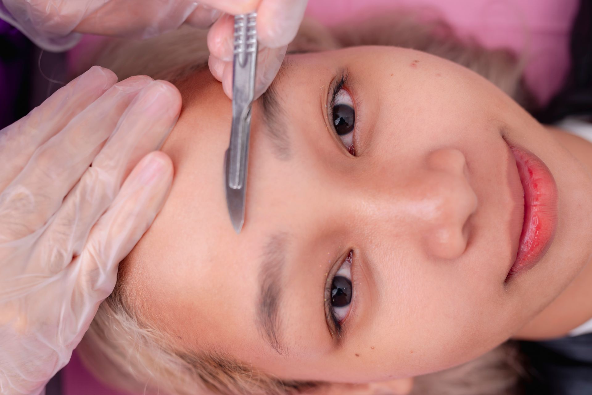 A woman is getting her eyebrows trimmed with a scalpel.