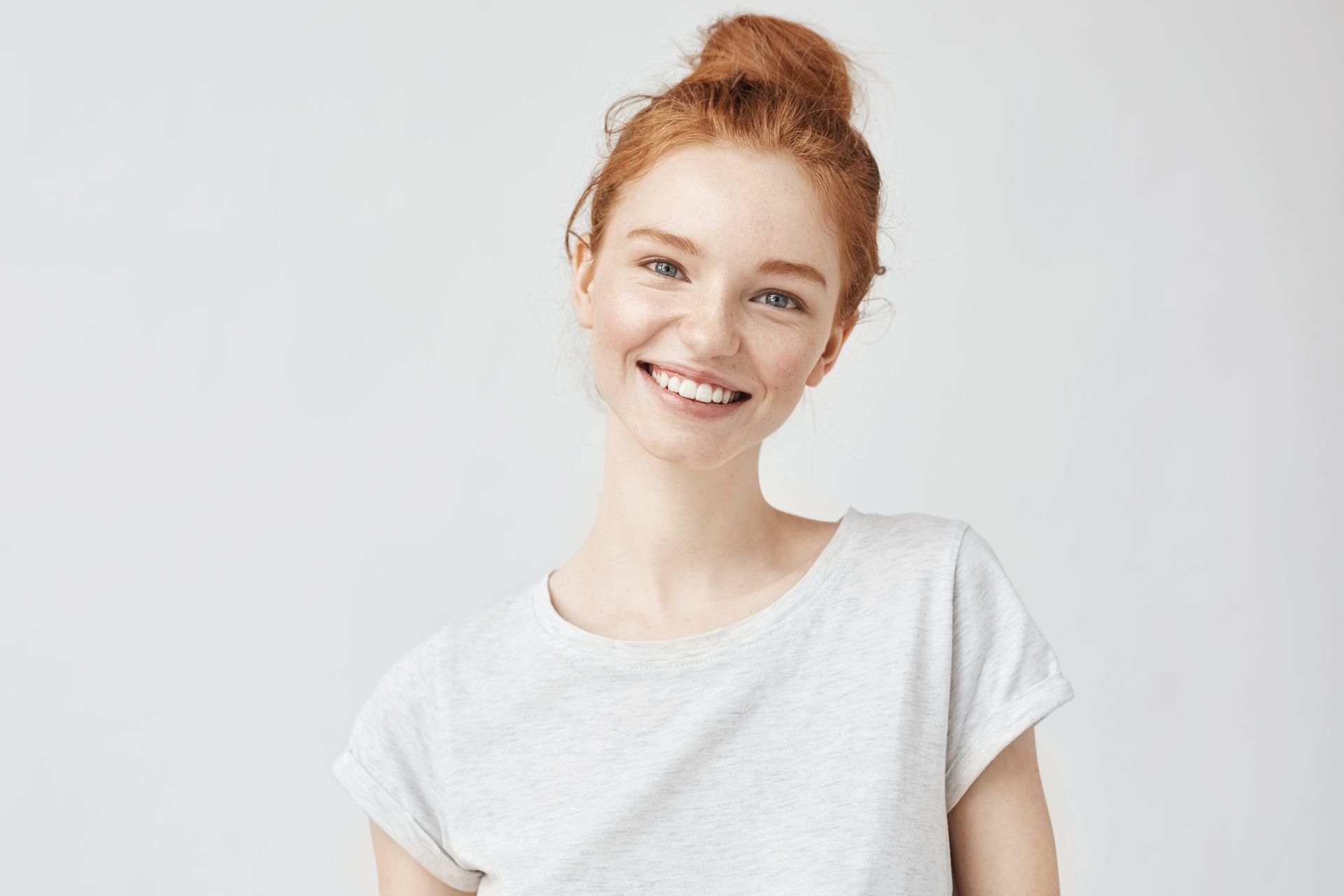 A woman with red hair is wearing a white t-shirt and smiling.