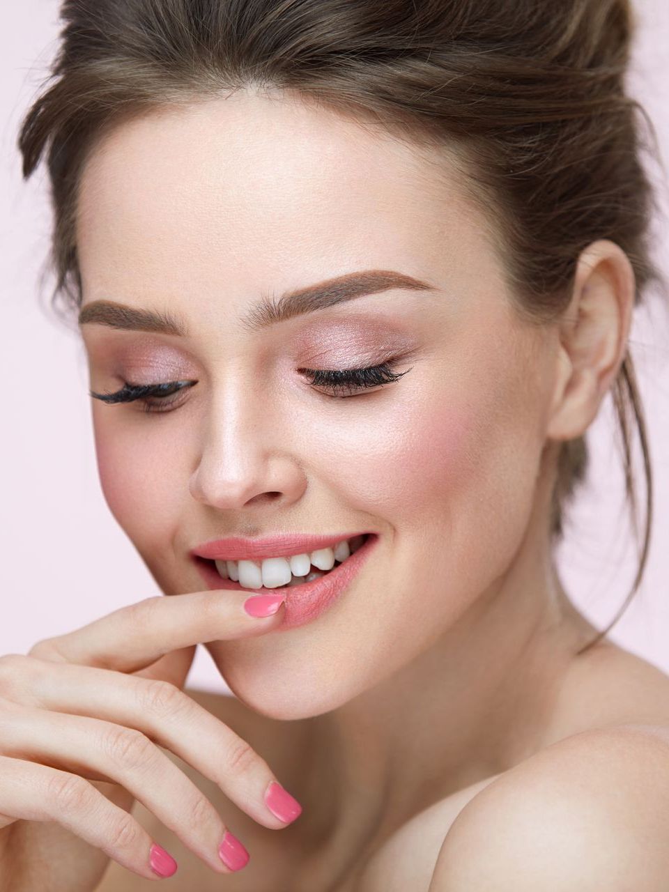 A woman with pink nails is smiling and touching her face.