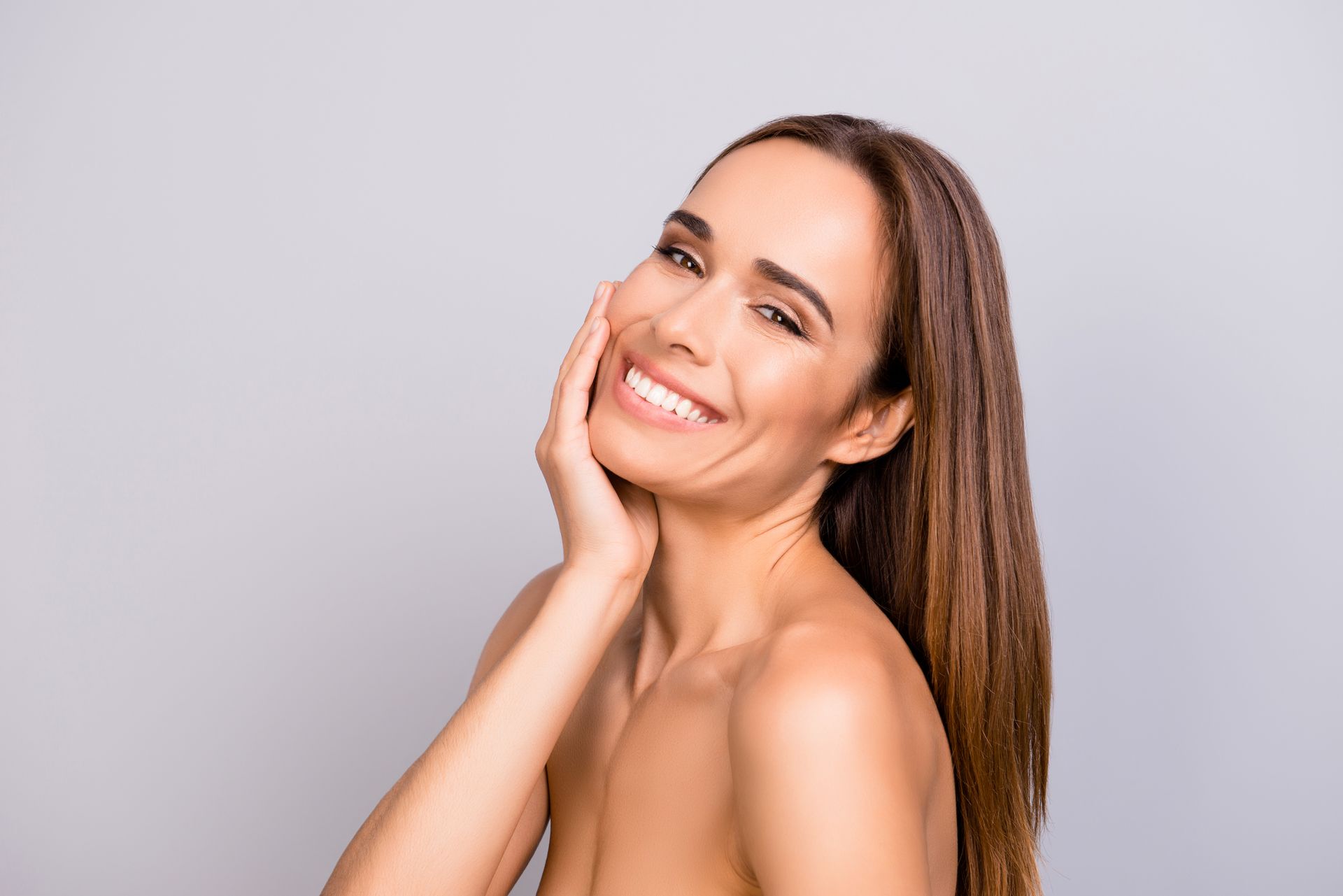 The woman is smiling and touching her face with her hand.