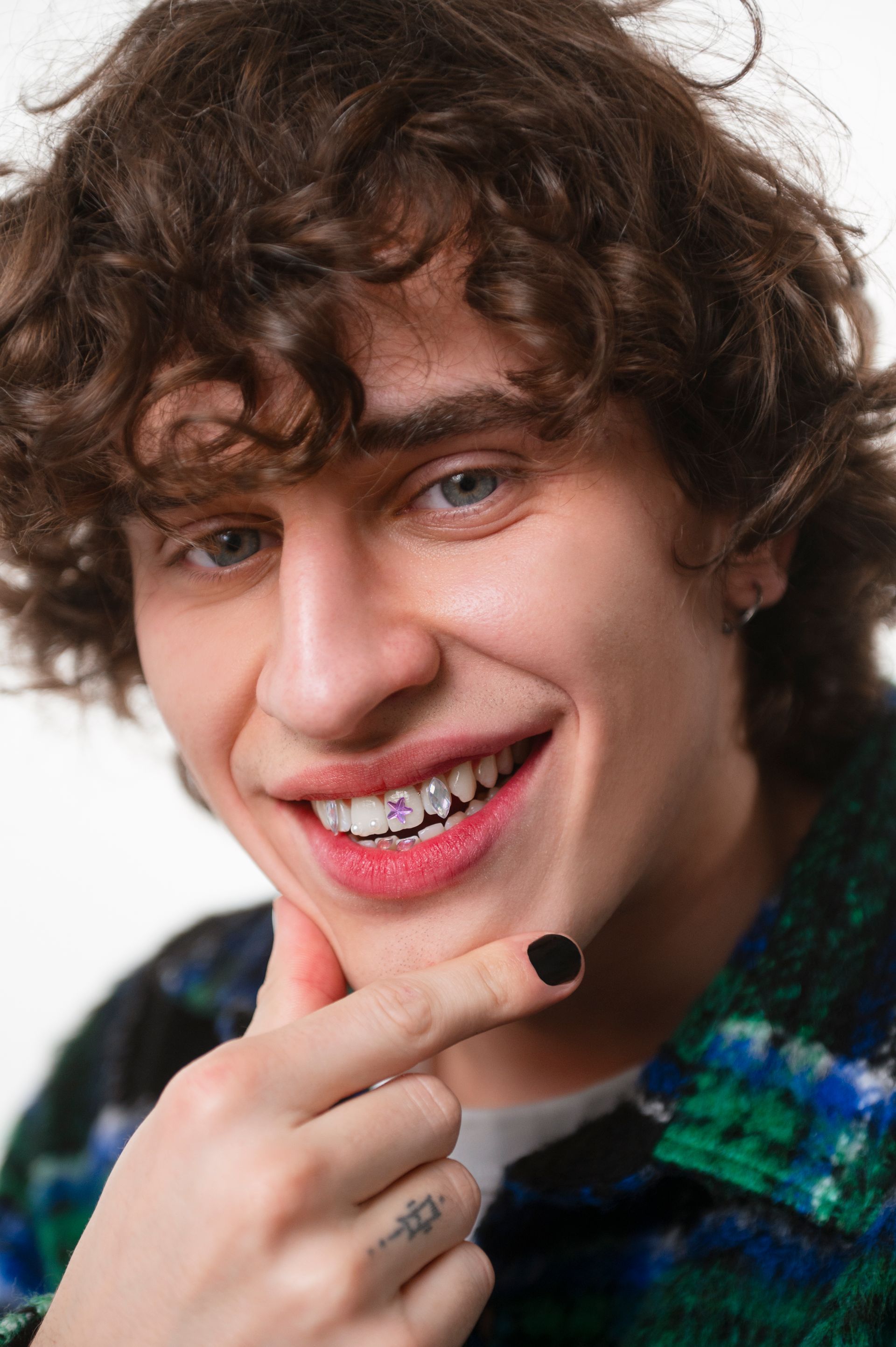 A young man with curly hair and braces on his teeth is smiling.