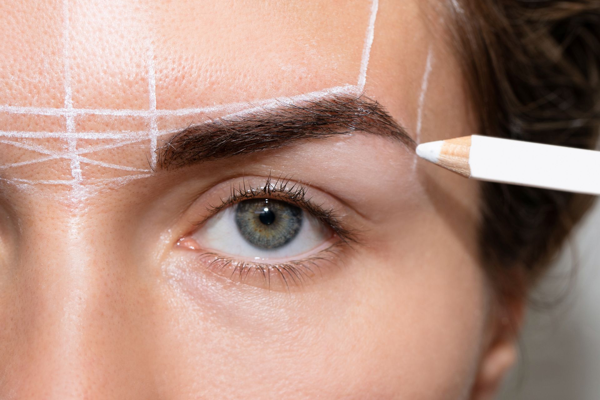 A woman is getting her eyebrows drawn with a pencil.