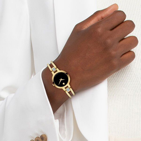 Een vrouw draagt een gouden horloge met een zwarte wijzerplaat en een diamanten accent aan de arm.