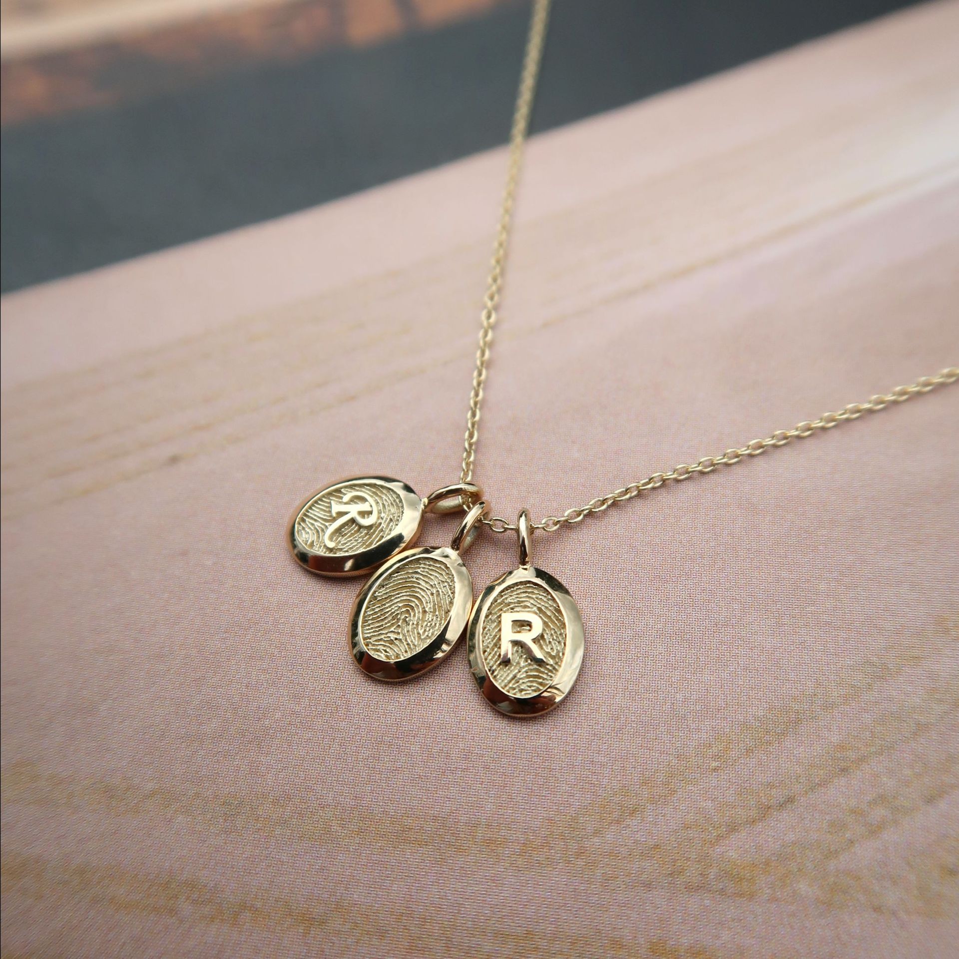 Gouden ketting met drie ovale hangers; degene rechts heeft de letter