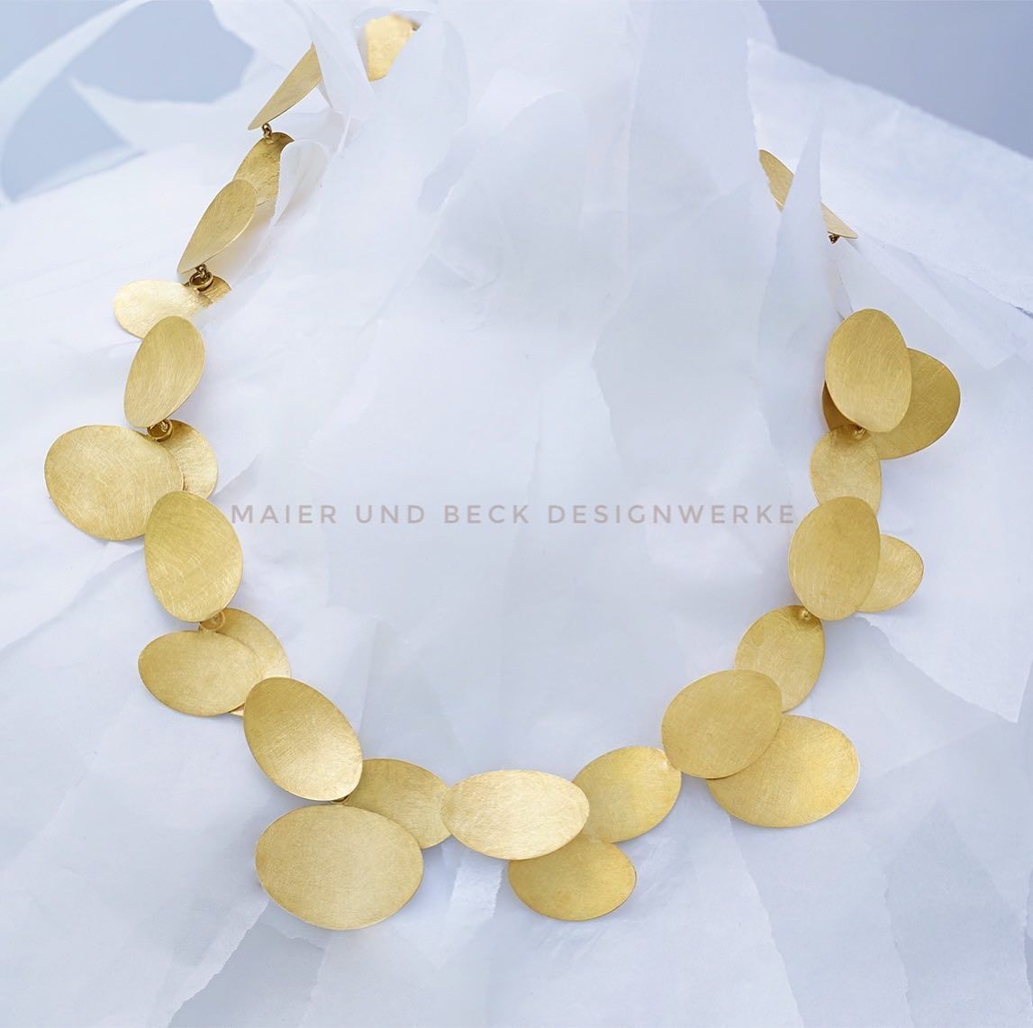 Gouden schijfketting op witte stof.