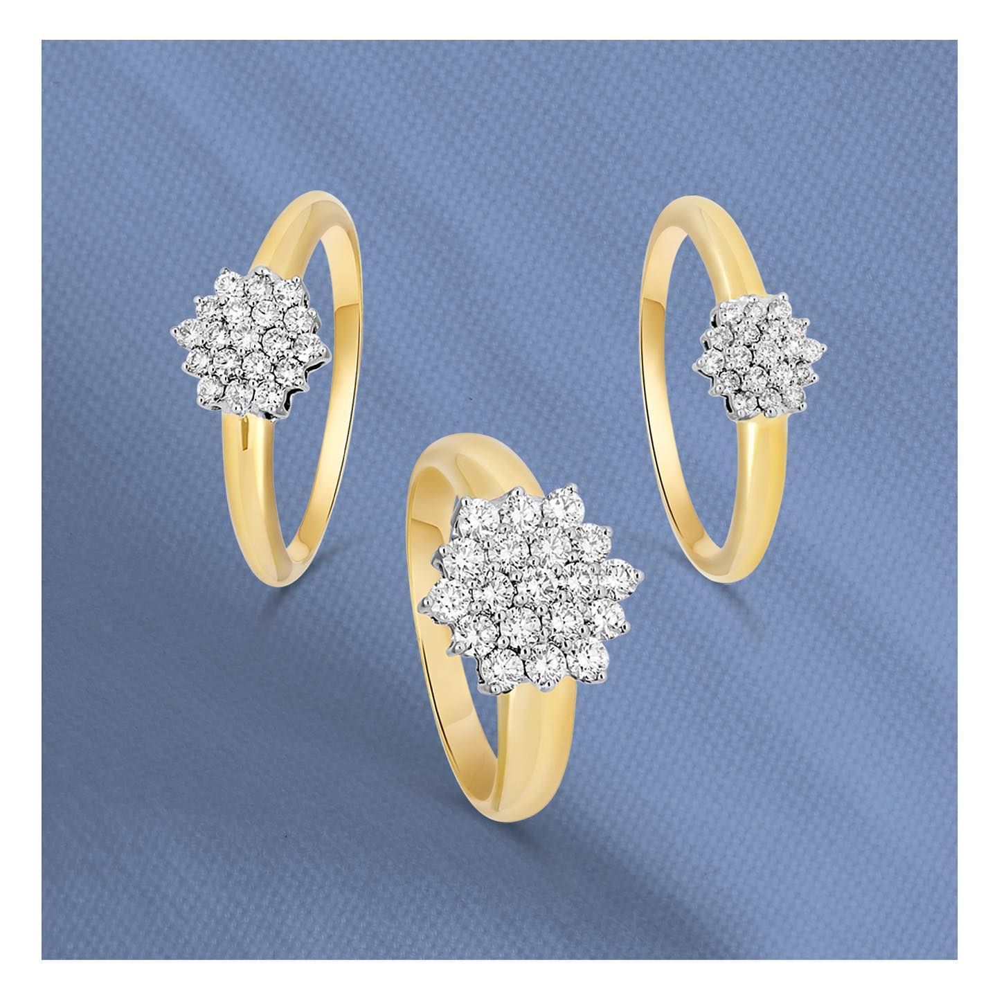 Drie gouden ringen met diamantclusters op een blauwe achtergrond.