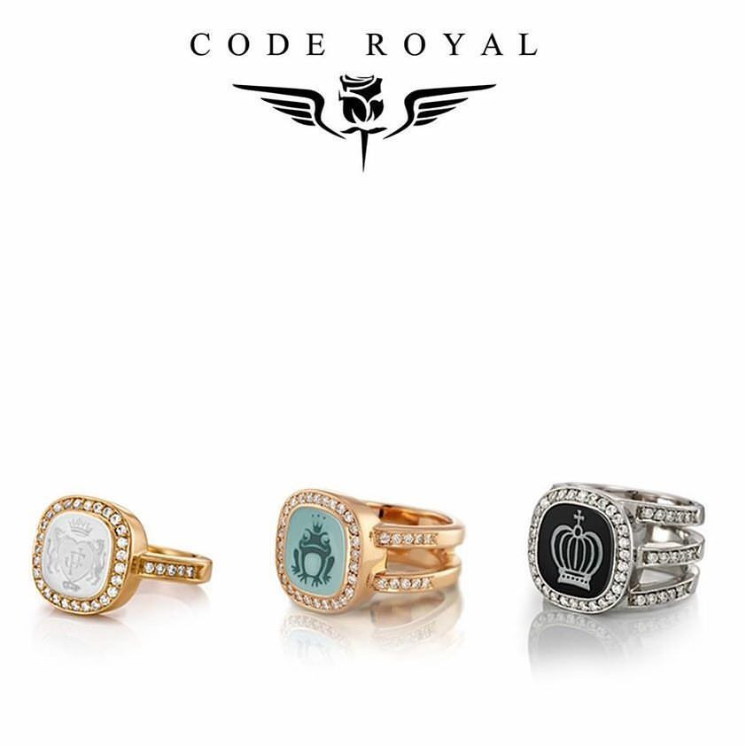 Drie sierlijke ringen met juweelkleurige centra en diamanten accenten onder een merklogo van een roos met vleugels.