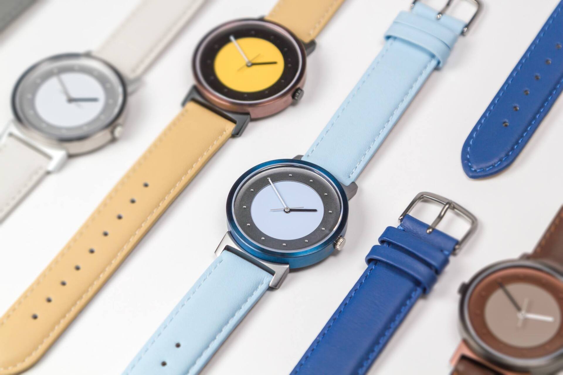 Close-up van verschillende polshorloges met verschillend gekleurde bandjes en wijzerplaten, tegen een witte achtergrond.