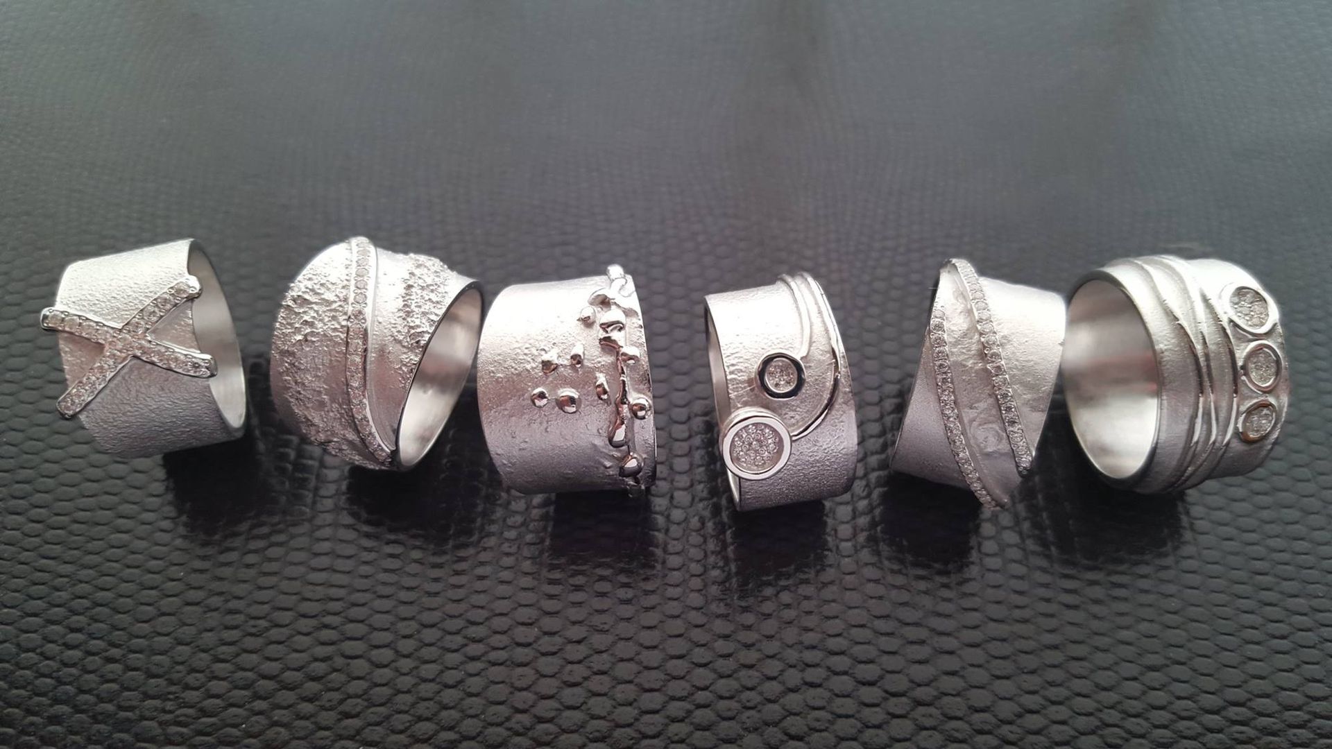 Zes zilveren ringen op een zwart oppervlak, elk met een unieke textuur en ontwerp.