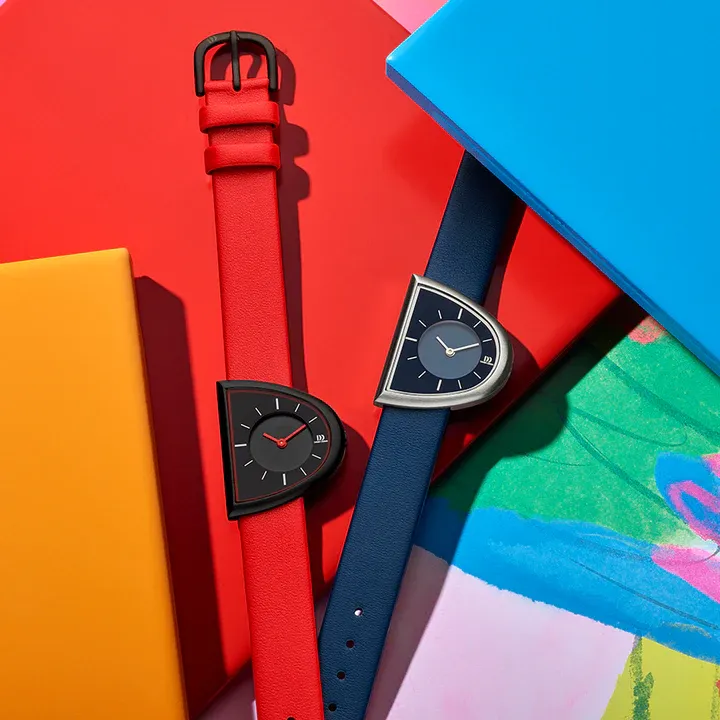 Twee unieke polshorloges met halfronde wijzerplaten; één rood en één blauw, tegen kleurrijke abstracte achtergronden.