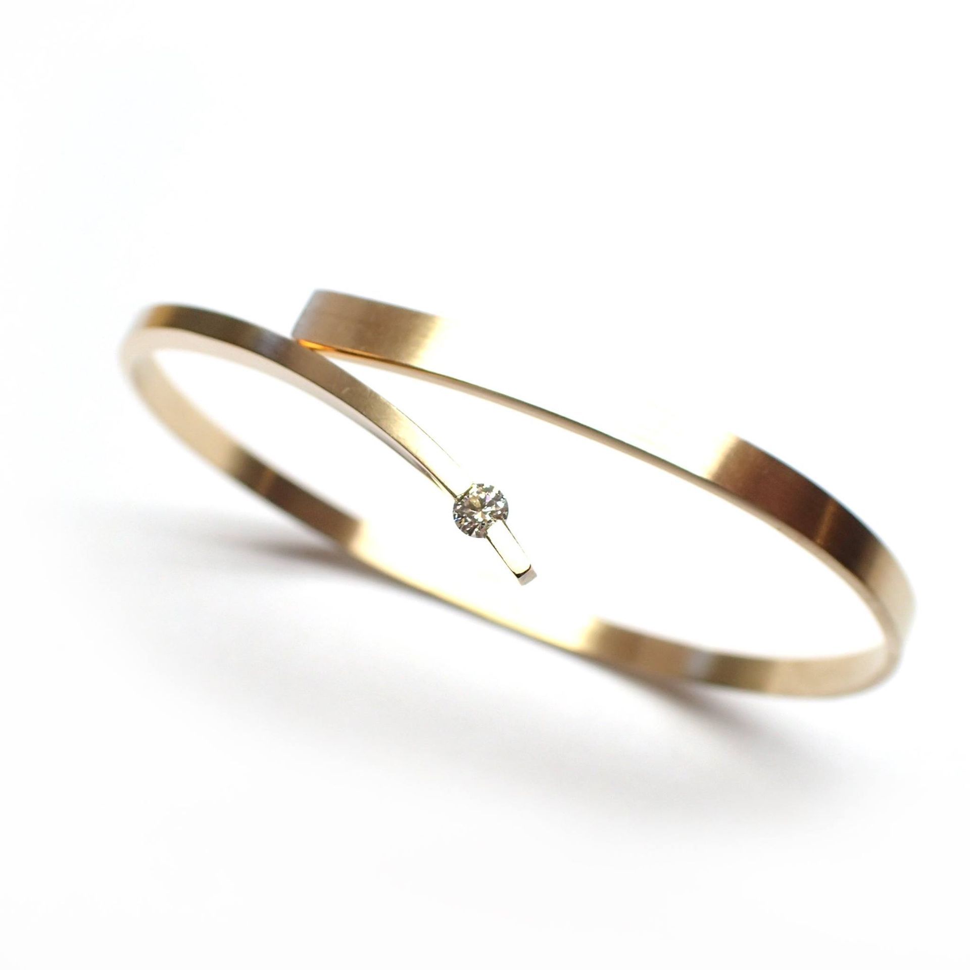 Goudkleurige armband met een gebogen ontwerp en een klein diamantje, waarschijnlijk een sieraad.