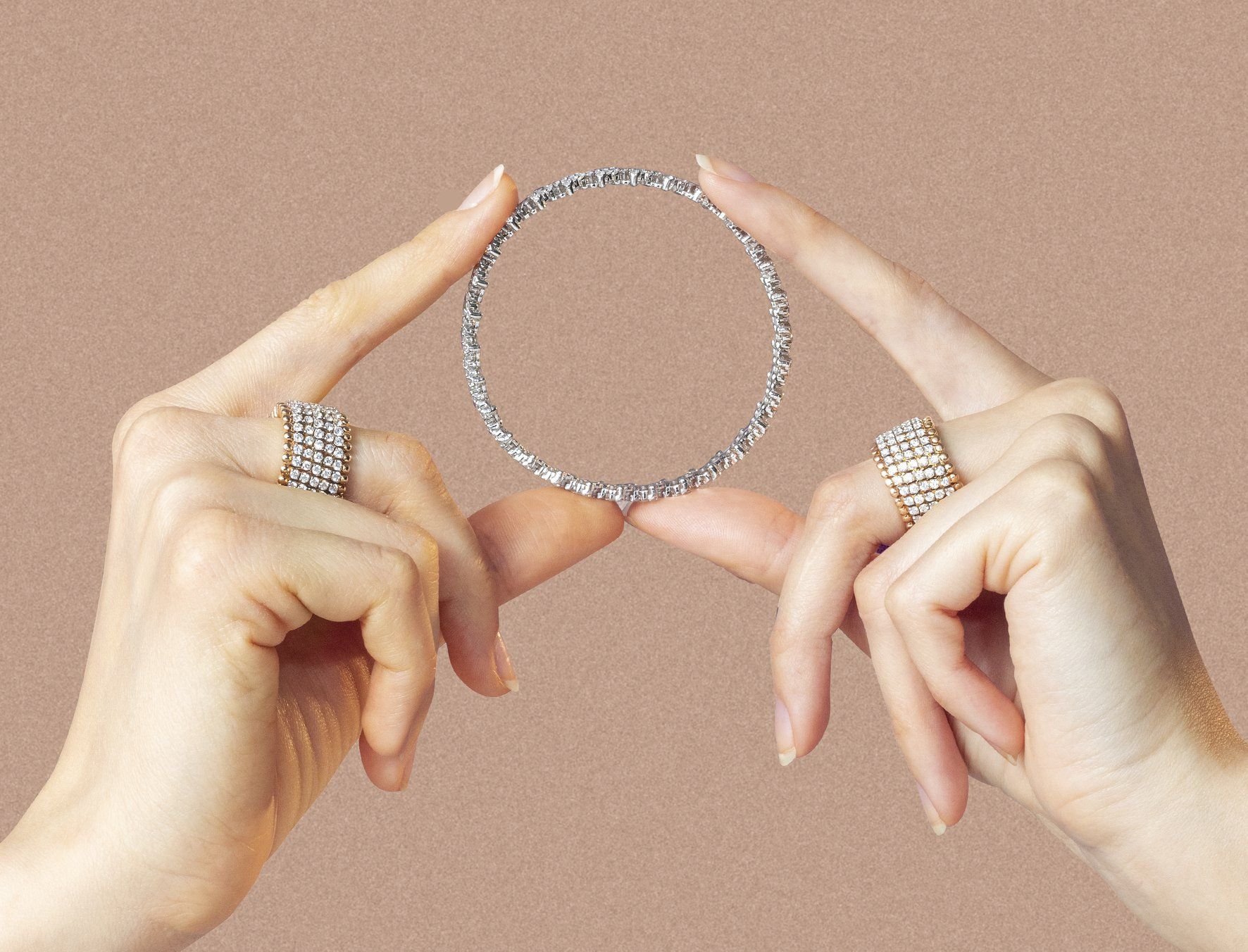 Handen houden een met diamanten bezette ketting vast, met diamanten ringen, tegen een beige achtergrond.