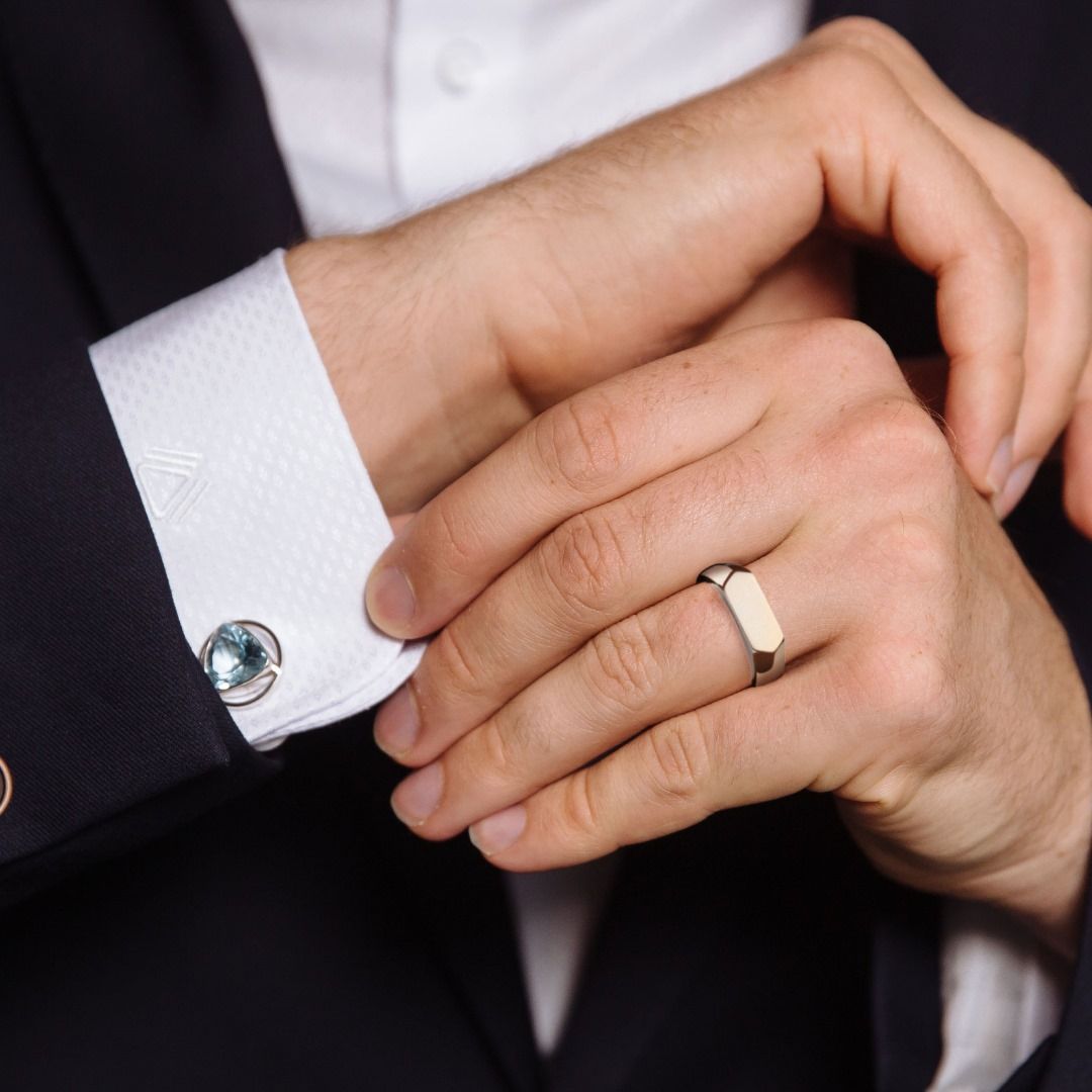 Man die een manchetknoop met een blauwe edelsteen en een rechthoekige zegelring aanpast.