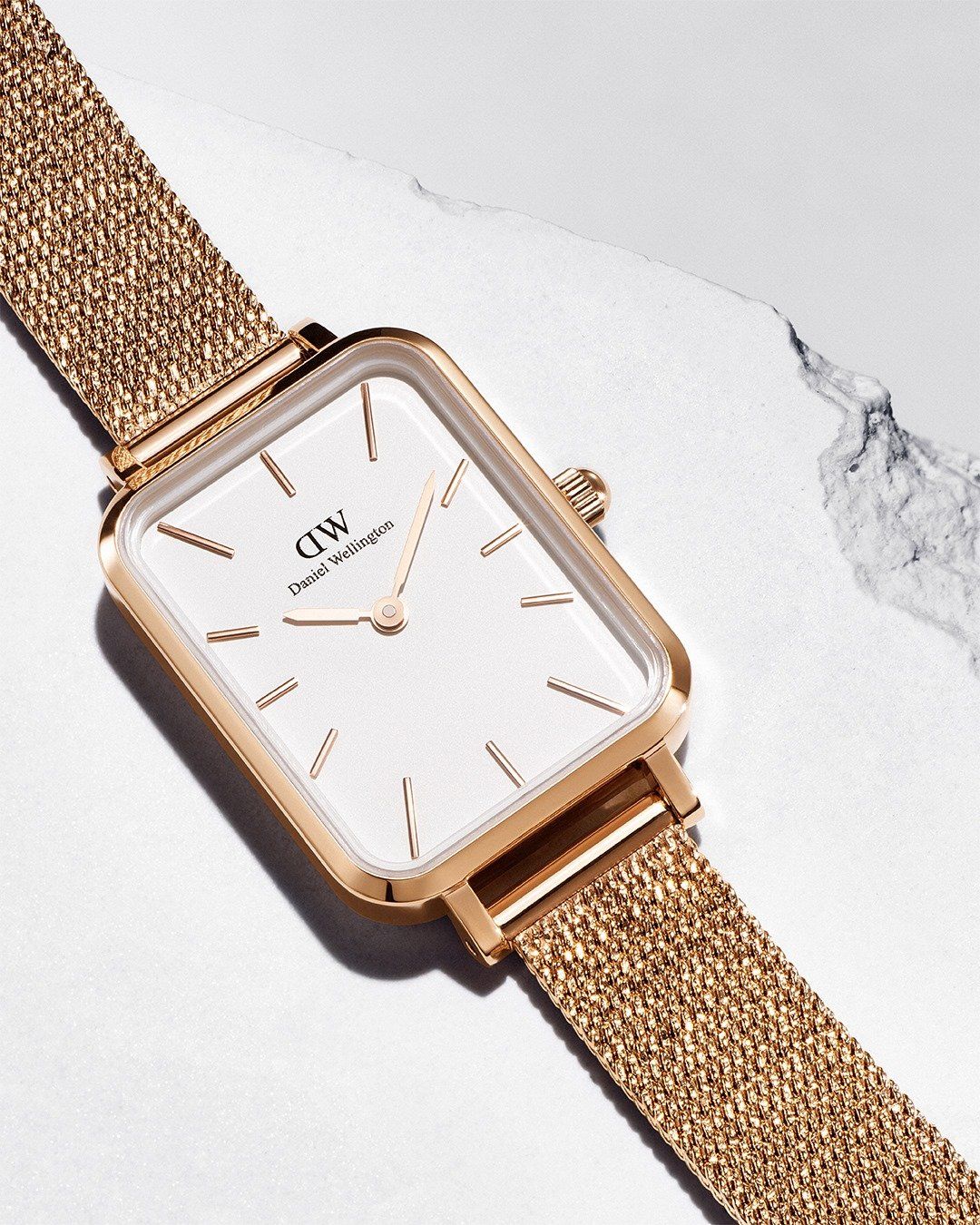 Rechthoekig Daniel Wellington horloge van goud met een meshband op een wit oppervlak.