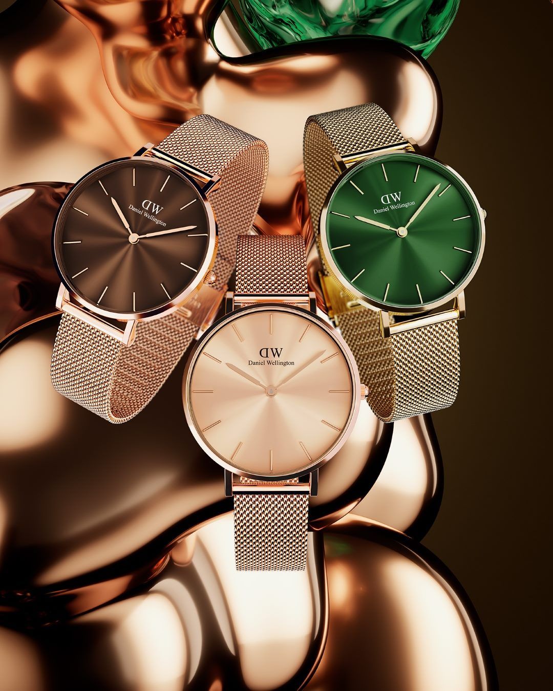 Drie horloges met mesh-bandjes in bruin, roségoud en groen op een gouden, reflecterend oppervlak.