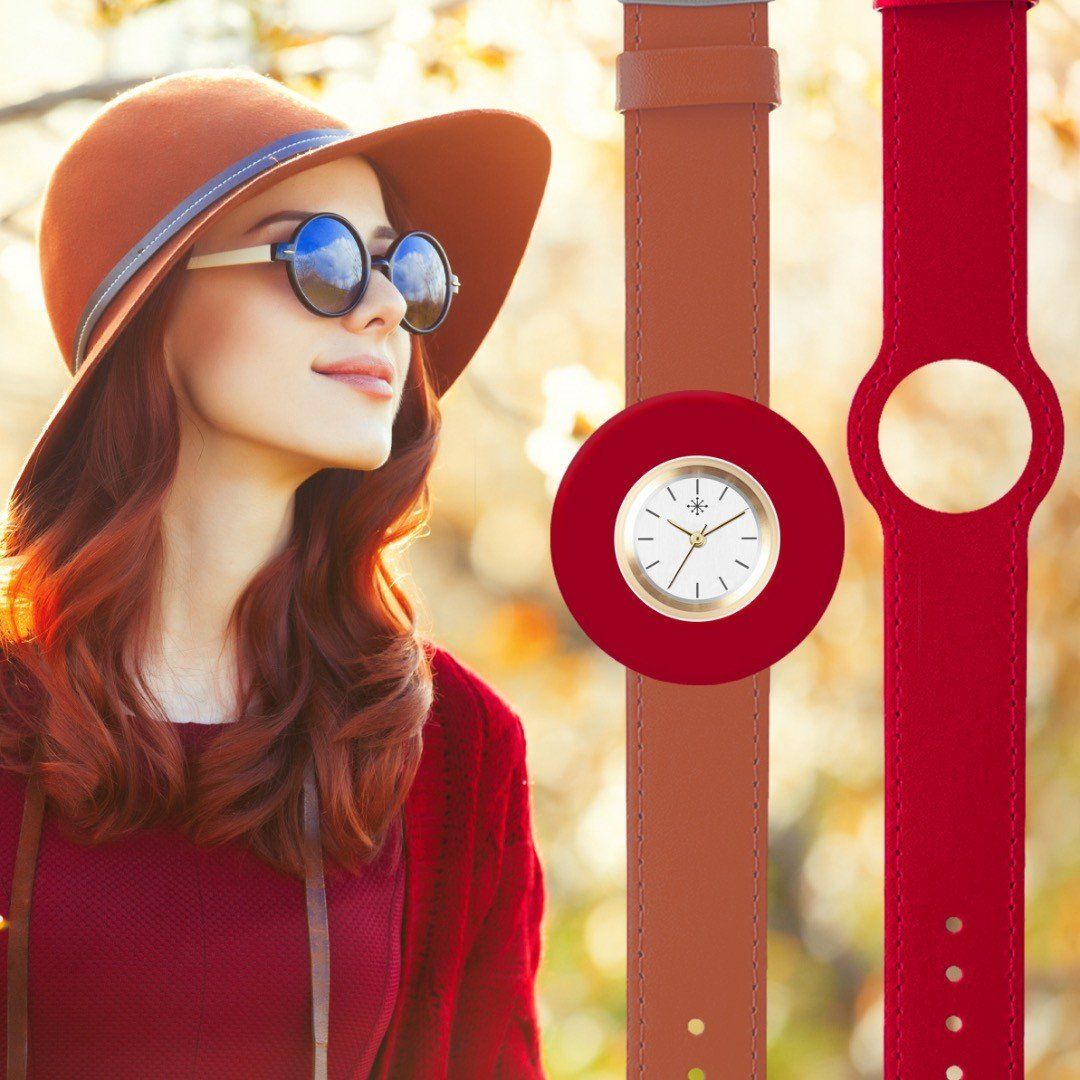 Vrouw met hoed en zonnebril, met een rood horloge en bandje, tegen de achtergrond van herfstbladeren.