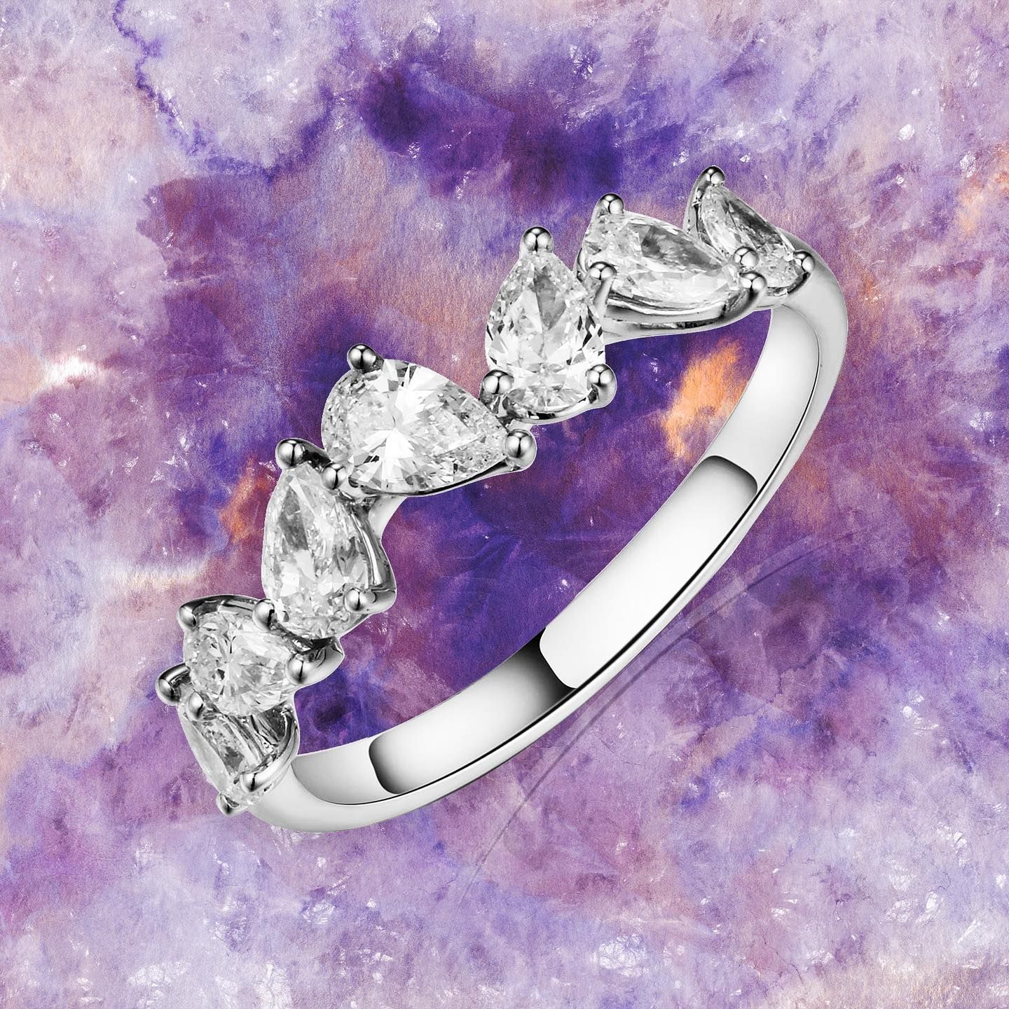 Zilveren ring met peervormige, heldere stenen op een paarse aquarelachtergrond.