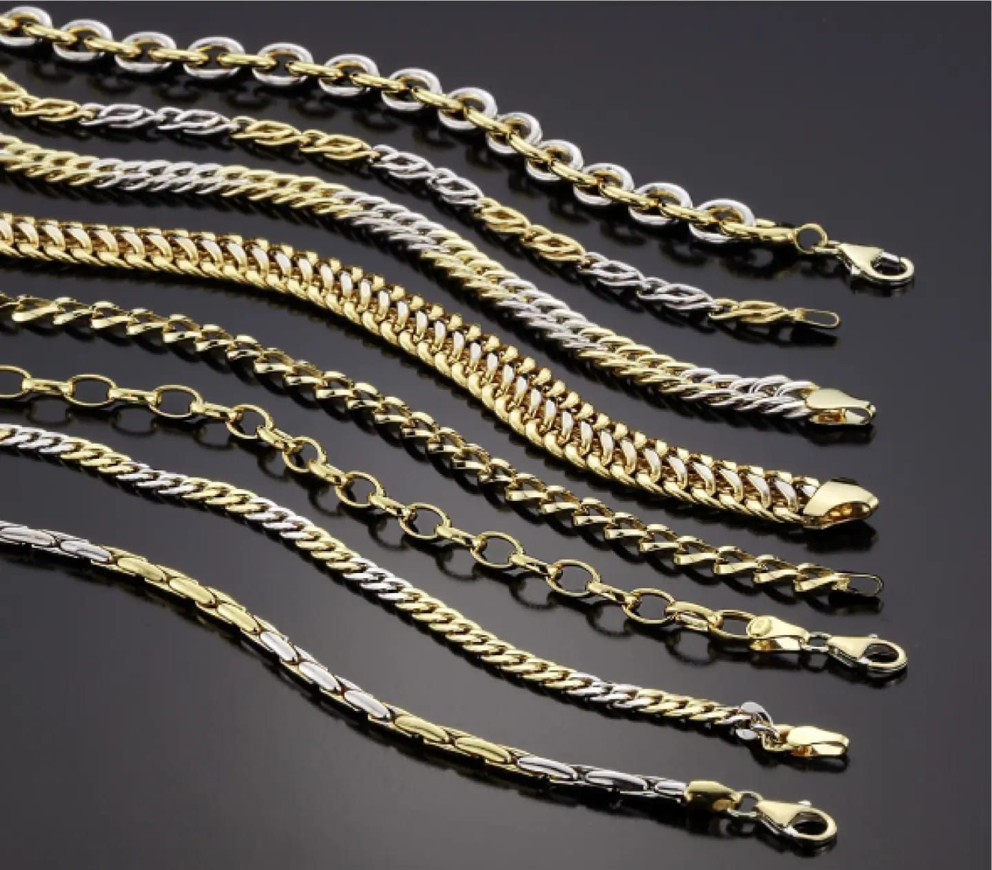 Armbanden van goud en zilver, diagonaal gerangschikt op een donker oppervlak.