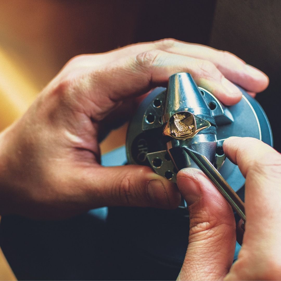 De handen van een juwelier werken aan een ring, die hij vasthoudt met een gereedschap en een klein pincet.