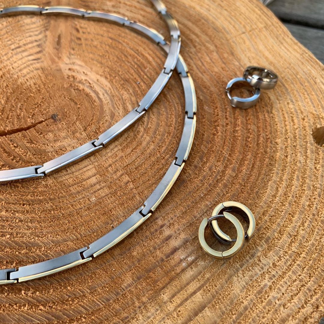 Zilveren en gouden sieraden op een houten oppervlak: een ketting en twee paar oorringen.