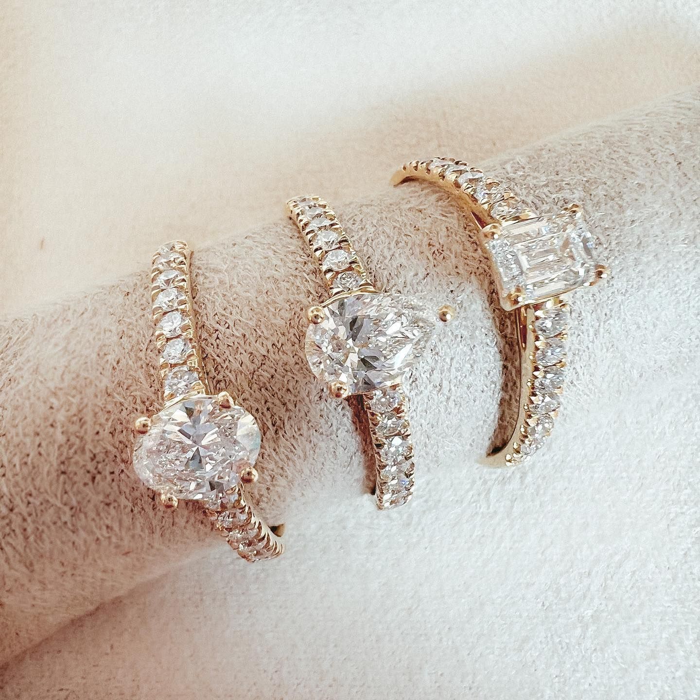 Drie verlovingsringen met diamanten op een wit oppervlak, met gouden banden en verschillende diamantvormen.