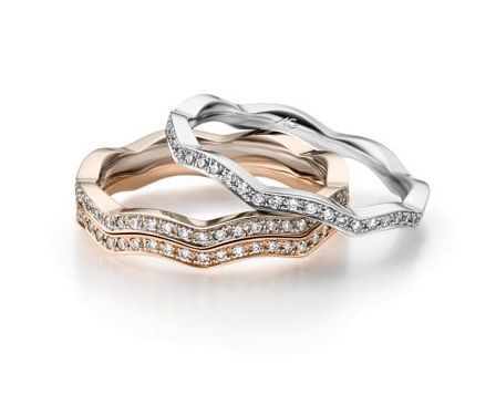 Drie golvende diamanten ringen, roségoud en witgoud, gestapeld op een witte achtergrond.