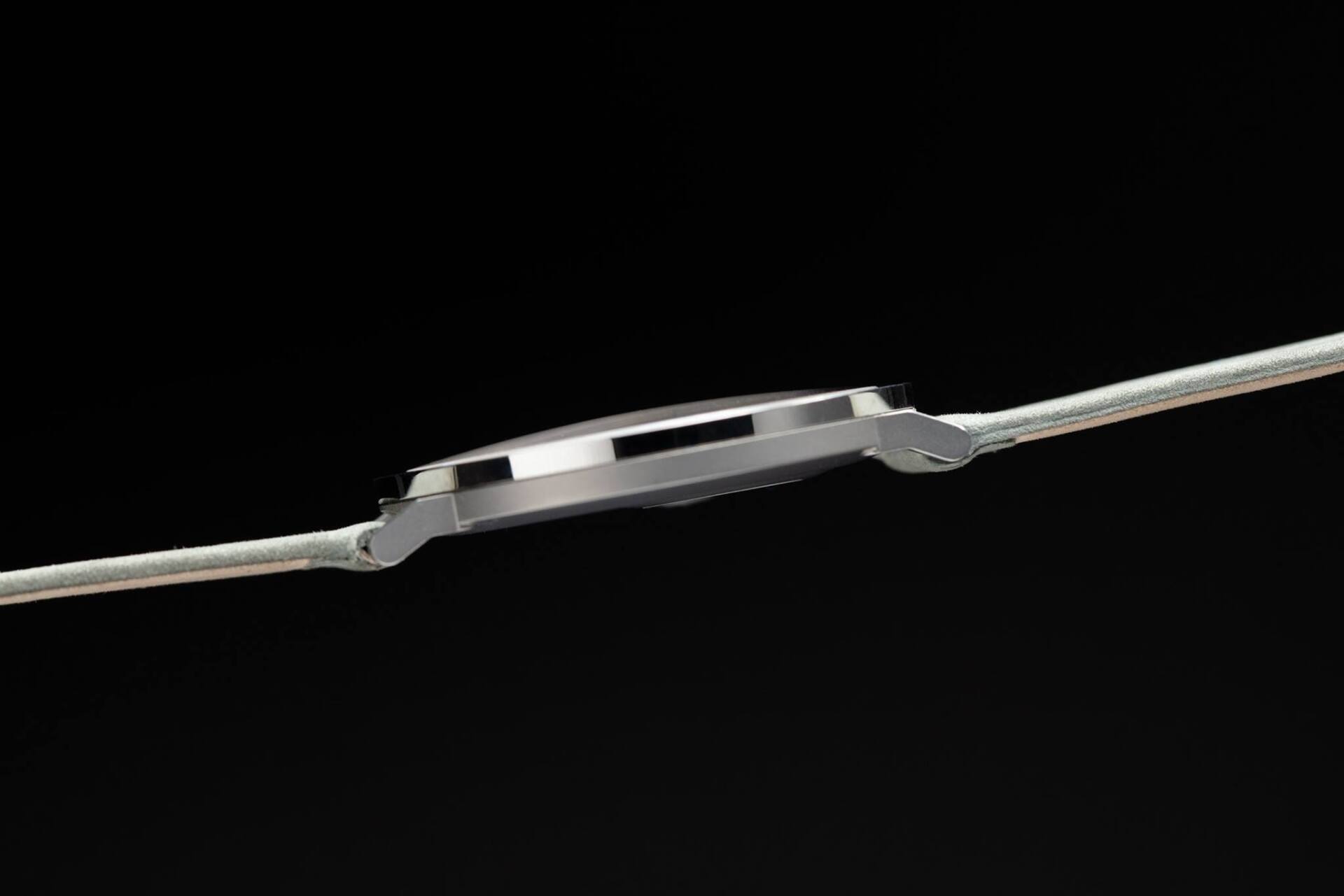 Zijaanzicht van een zilveren polshorloge met een dun profiel en een meshband tegen een zwarte achtergrond.