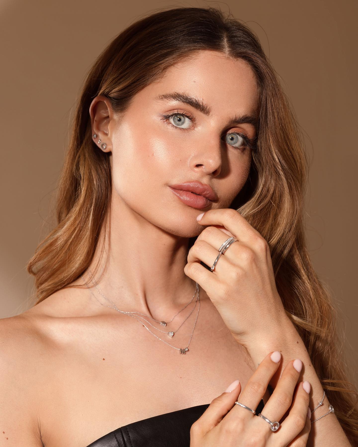 Vrouw met blond haar, lichte huid en blauwe ogen, draagt ​​sieraden en kijkt de toeschouwer aan.