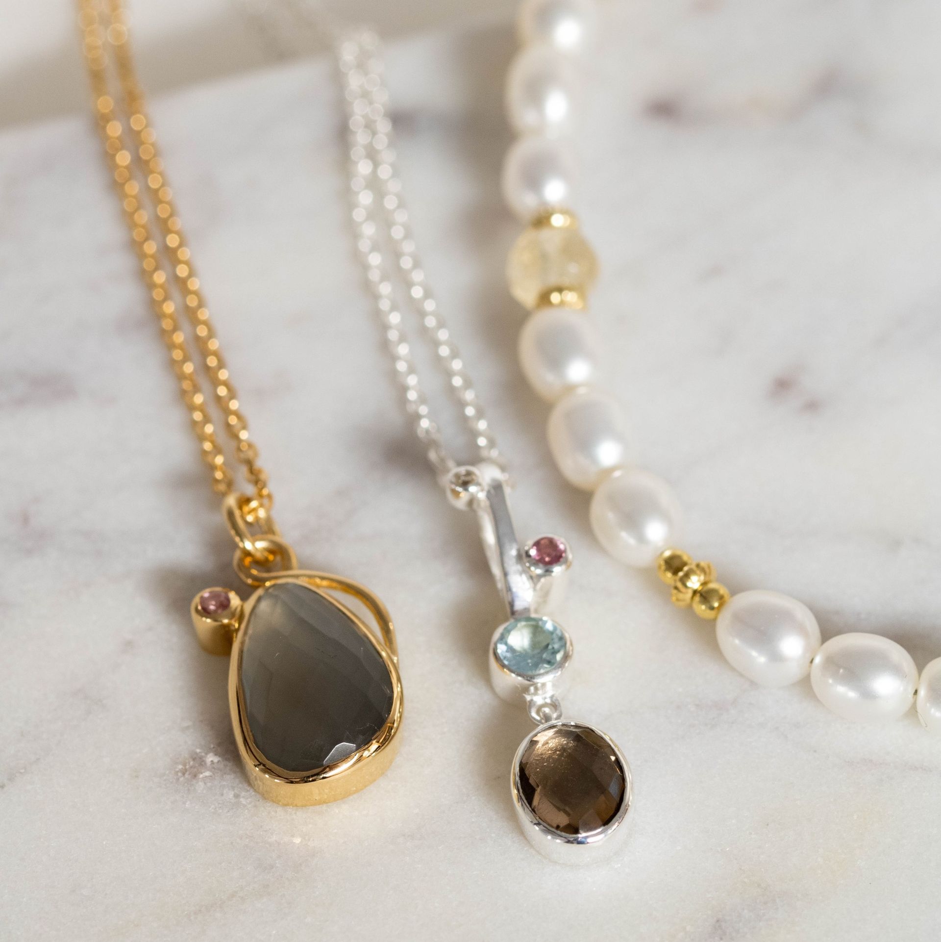 Drie kettingen: gouden en zilveren kettingen met edelsteenhangers en een parelsnoer.