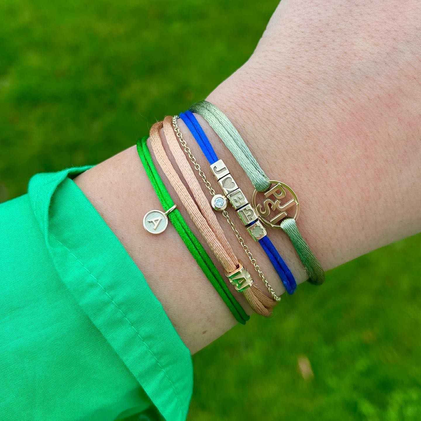 Pols met een stapel kleurrijke armbanden: groene, roze, blauwe en gouden accenten.