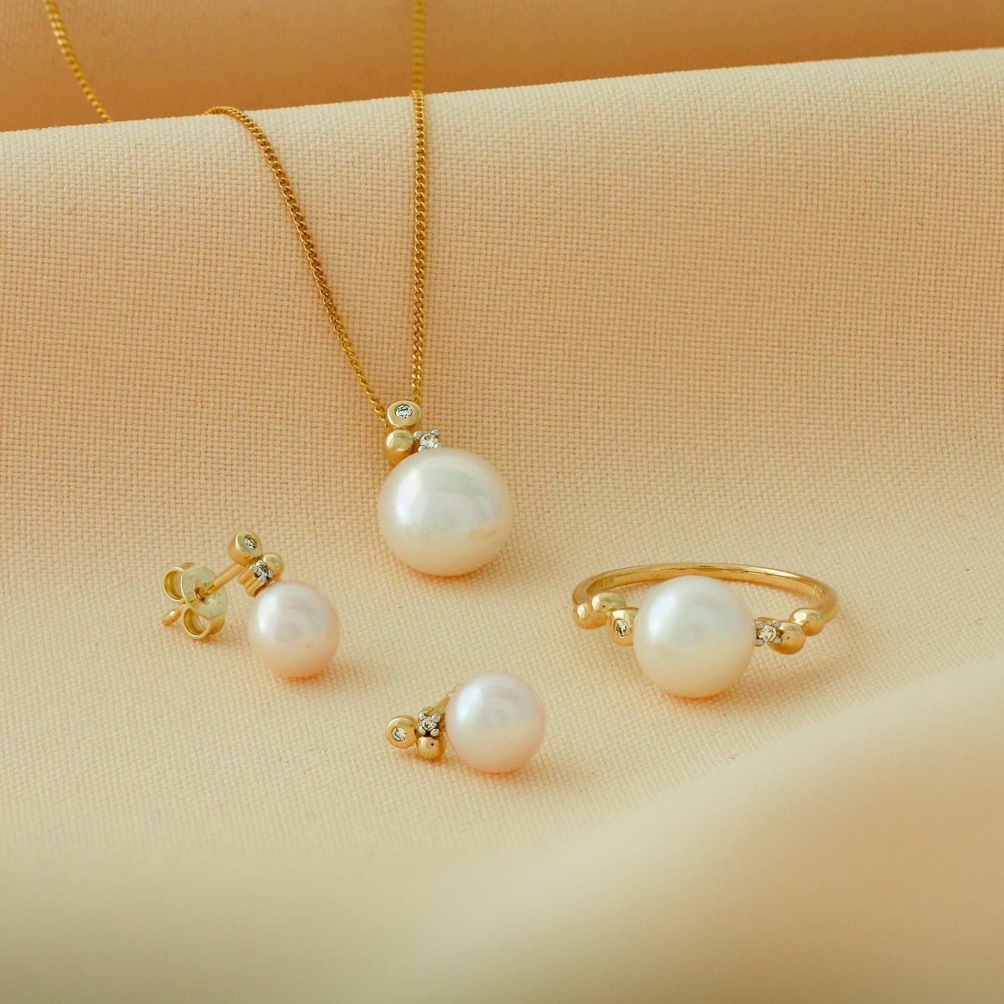 Parelsieradenset op een perzikkleurige achtergrond: ketting, oorbellen en ring.