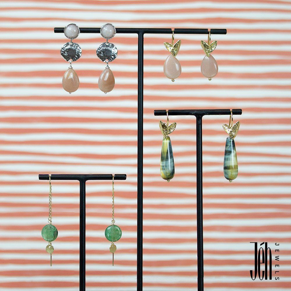 Oorbellen op een zwarte displaystandaard tegen een perzikkleurige achtergrond.