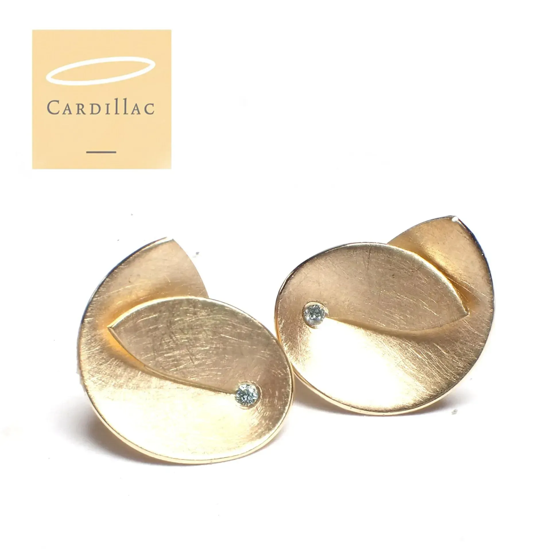 Goudkleurige, abstracte oorbellen met kleine blauwe edelstenen, naast een logo.