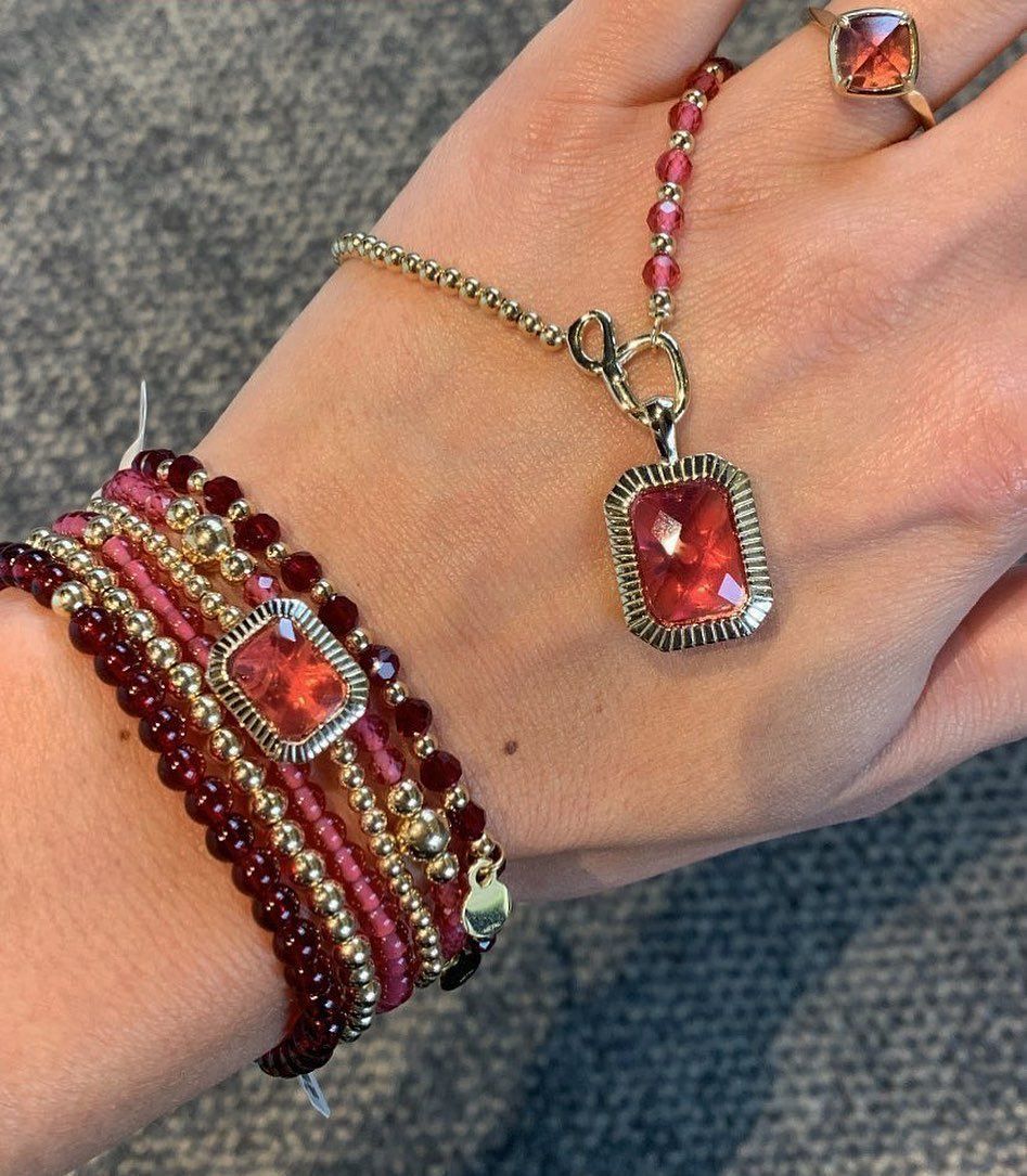 Hand met rode en gouden sieraden: armband, ketting en ring.