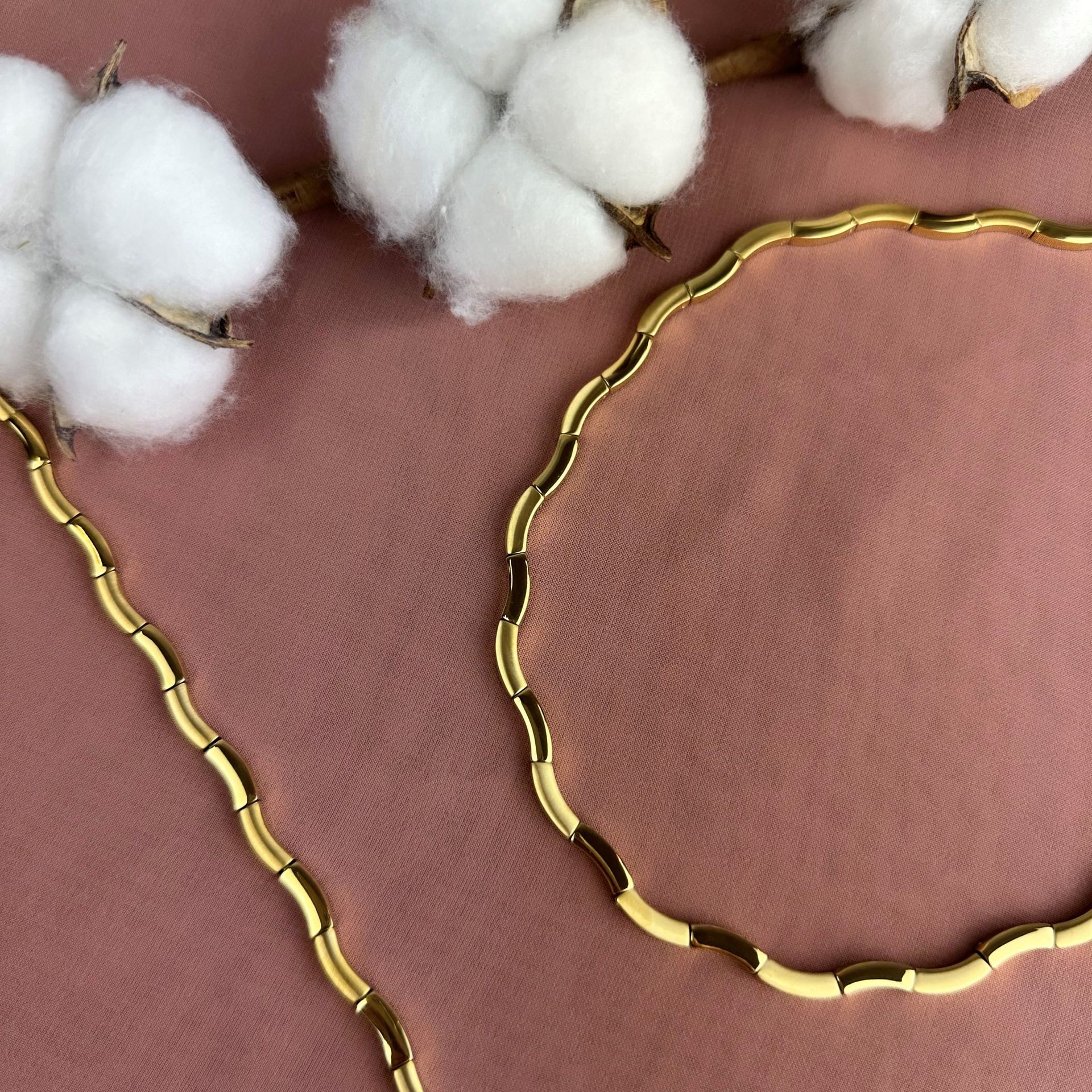 Gouden ketting en katoenen bloemen op een roze ondergrond.
